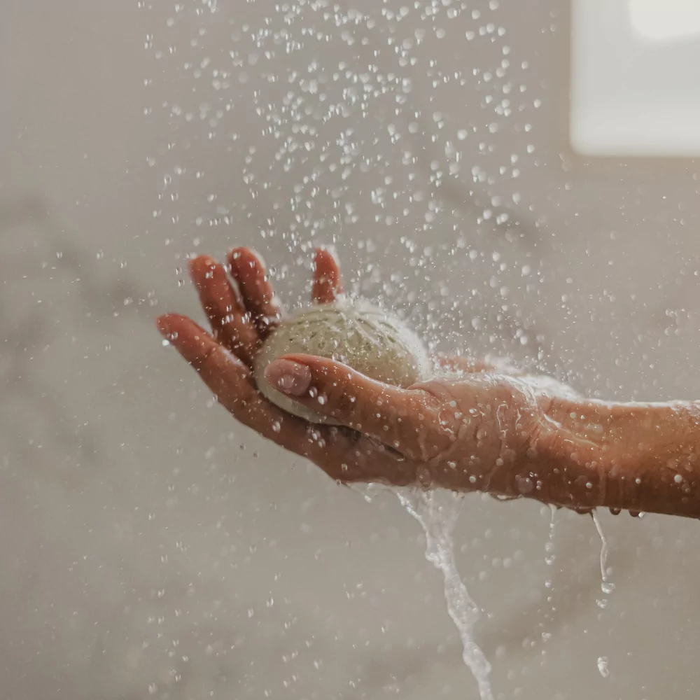 Le fond du visuel est le mur d'une salle de bain marbrée. On y voit une main sous l'eau qui met en avant le shampoing Solide Pondichéry