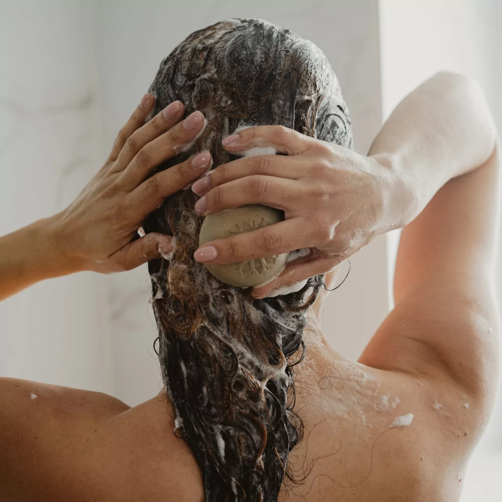 Le visuel met avant une personne de dos en train de faire mousser ses cheveux avec le shampoing solide Pondichéry de Couleurs Gaïa