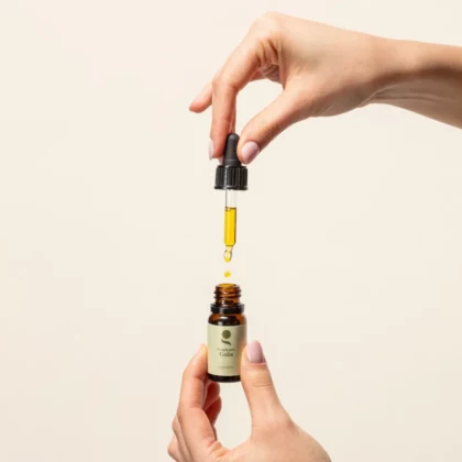Quintessence cuivrée, le complexe d’huiles essentielles certifié bio pour des reflets cuivrés de 10ml est ouvert. Le récipient est tenu par une main, l'autre main tient la pipette, montre la couleur du produit et sa texture grâce au compte goutte.