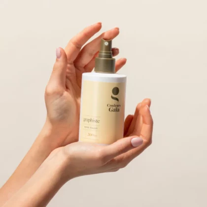 Graphiste, le spray fixant naturel de150ml est tenu par deux mains de femme.