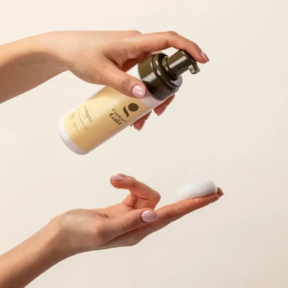 Volupté, la mousse coiffante certifiée bio de 150ml est tenue dans une main au dessus d'une main qui contient de la mousse du produit mettant en avant la texture et sa couleur.