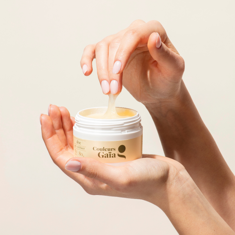 Pot Aloe Gel coiffant certifié bio 80g, posé sur une main. L'autre main retire ses doigts du pot afin de montrer la texture du gel coiffant.