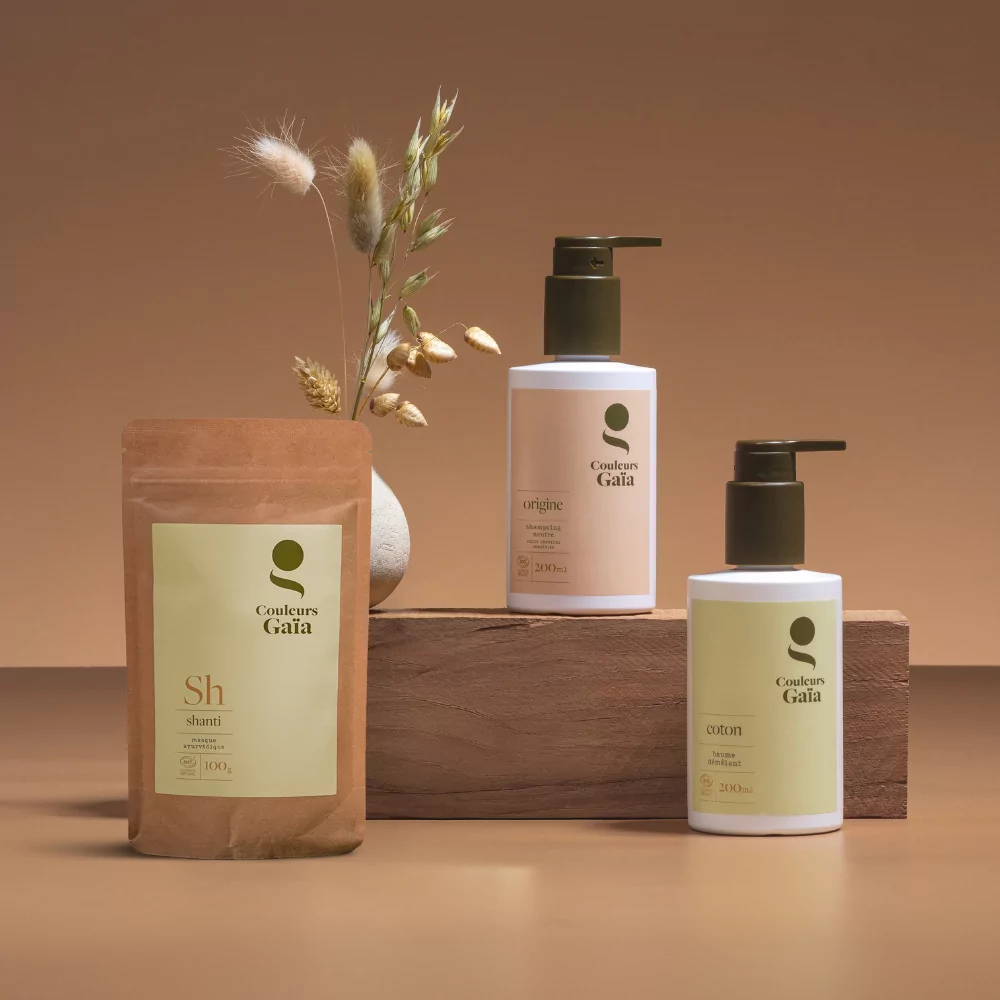 le visuel met en avant 3 produit recommandés par Couleurs Gaïa pour les cuirs chevelus sensibles. Le fond est de couleur marron, l'ambiance est végétale, naturelle. Le masque Shanti, le shampoing origine et le baume coton Couleurs Gaïa sont mis en avant.