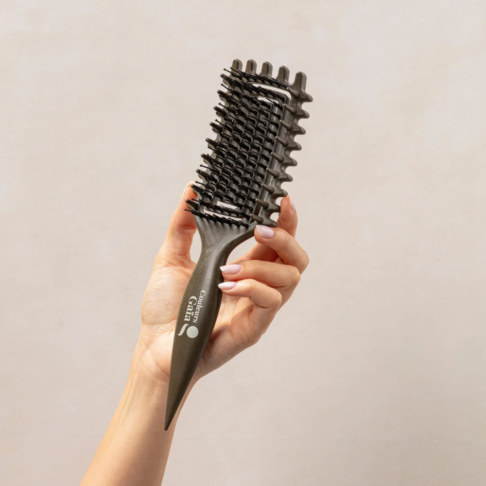La brosse Couleurs Gaïa pour cheveux bouclés, de couleur kaki avec sérigraphie blanche, est présentée dans une main